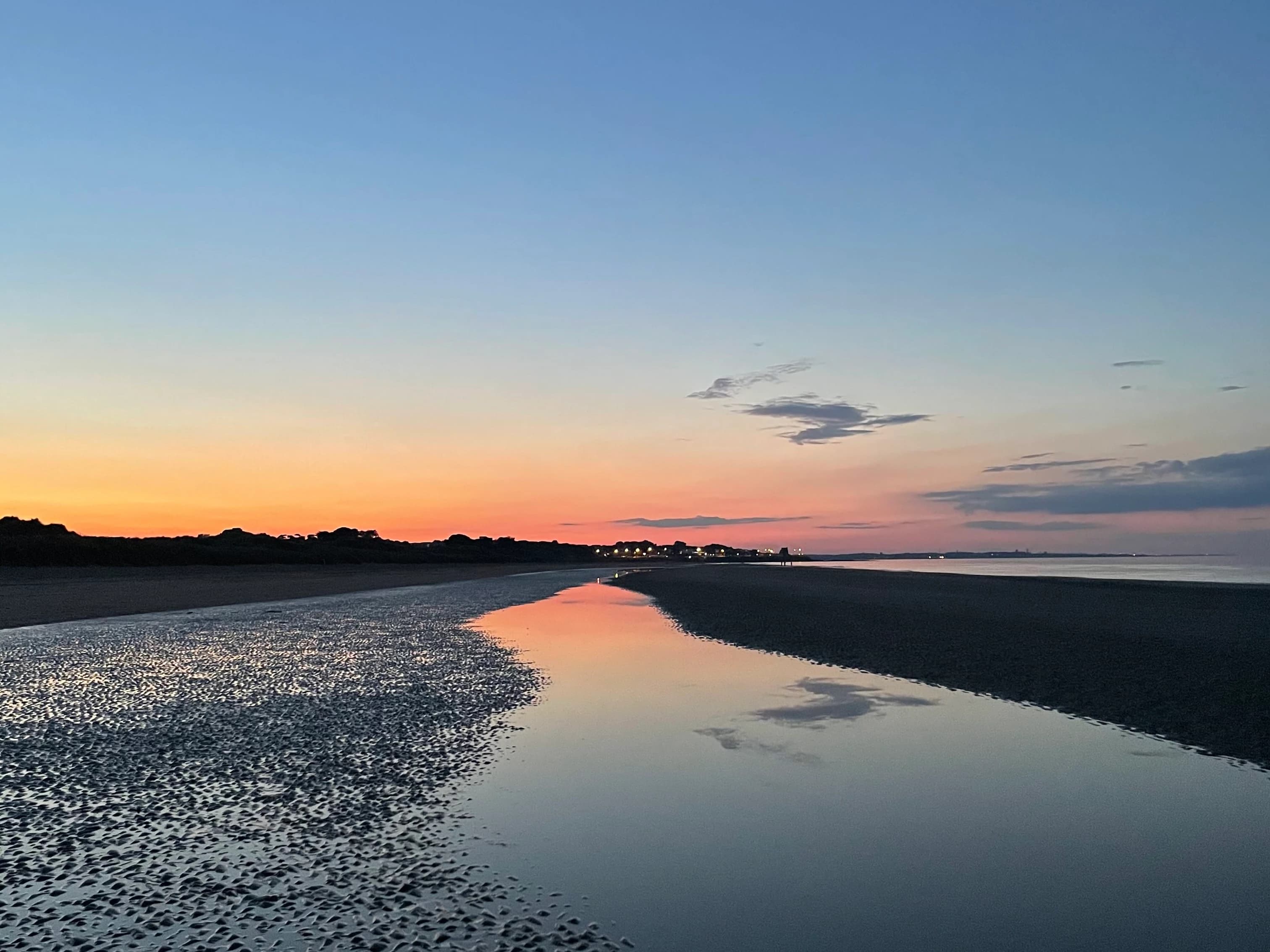Sunset reflection on tidal beach with rippled sand patterns